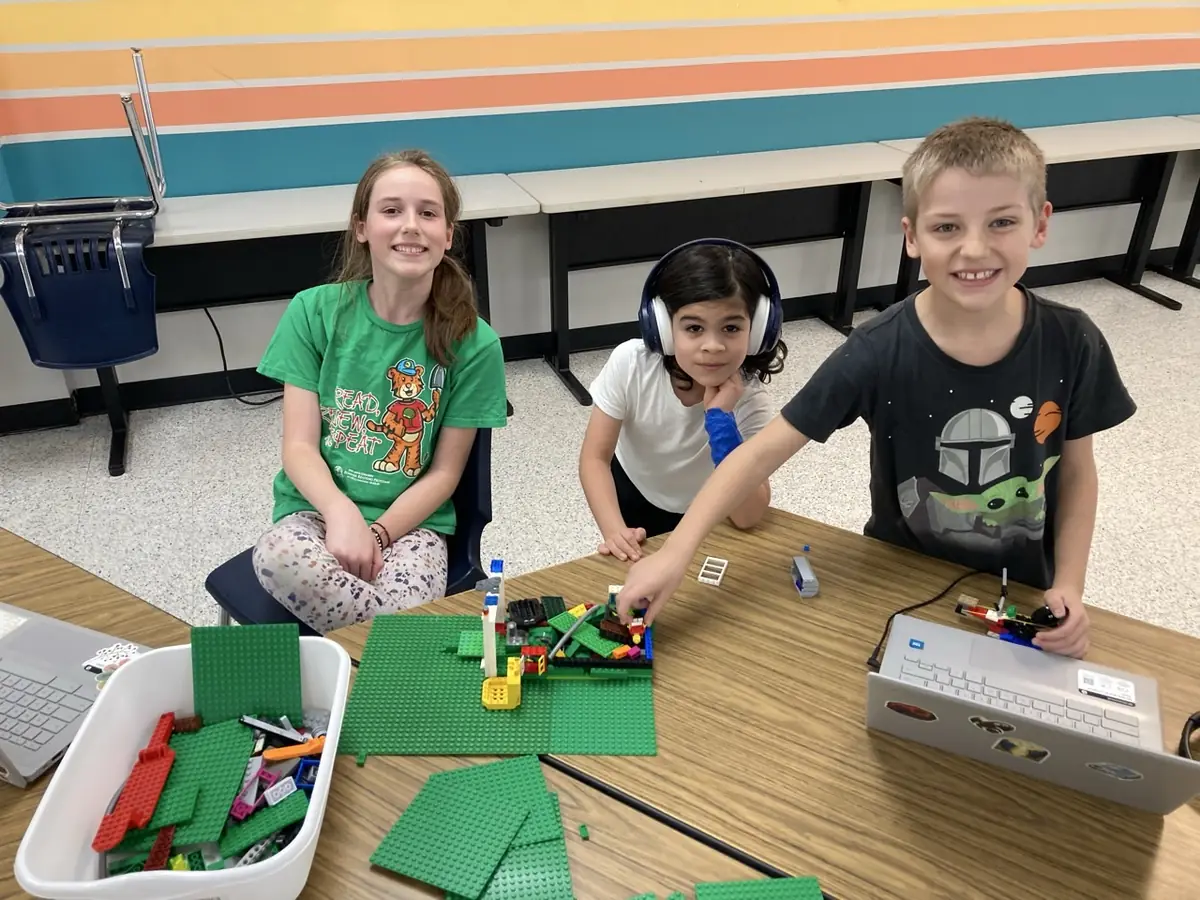 Learners build with LEGO bricks at a table beside an open laptop.